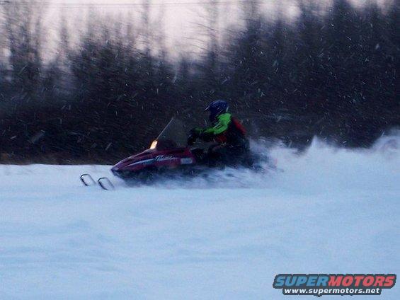 Red snowmobile with rider in motion, kicking up snow