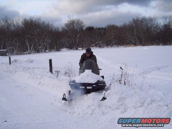 Snowmobile partially covered in snow with a person on it, outdoors in a snowy landscape