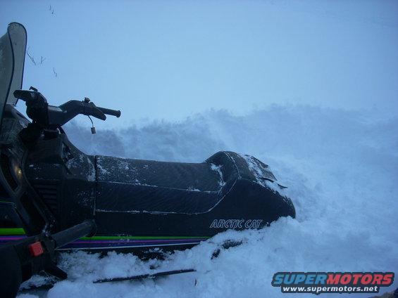 Black snowmobile with green and purple stripes in deep snow, "ARCTIC CAT" visible on the side