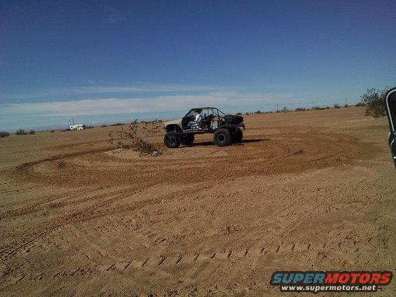 Buggy with roll cage driving in sandy terrain. Spare tire mounted on back