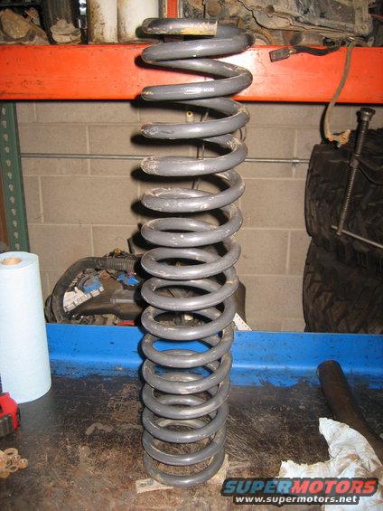 Gray coil spring on a workbench with tools and a roll of paper towels
