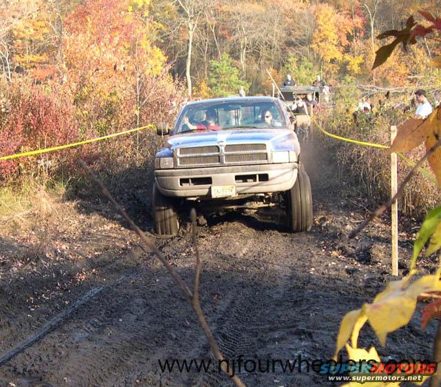 Dodge Ram pickup truck with lifted suspension driving through mud, other vehicles and people in background