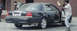 1999 Mercury Grand Marquis - A black sedan is seen from the rear as a man fires a weapon from the open driver's side door.