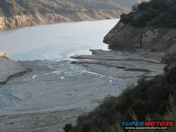 Dry riverbed leading to a lake with rocky hillsides