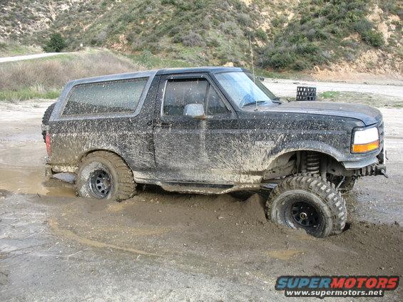 Muddy black SUV stuck in a mud pit, front right wheel submerged