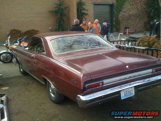maroon coupe parked outside, motorcycle nearby, people standing around
