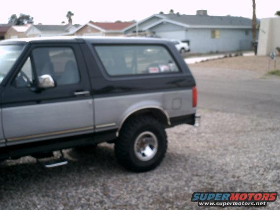 Side view of a two-tone gray and black Ford Bronco parked on a gravel lot