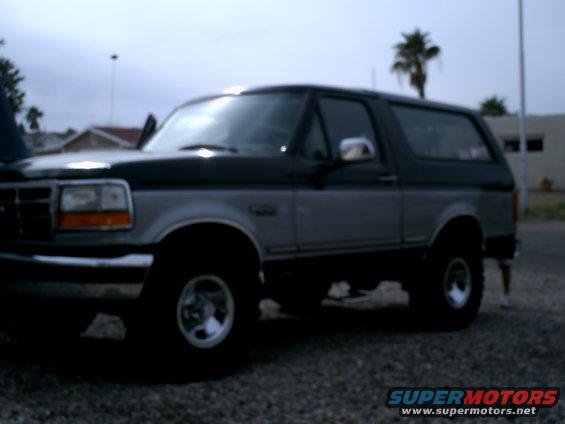 Two-tone gray and black Ford Bronco SUV, side view, with aftermarket wheels and a slightly open driver's door