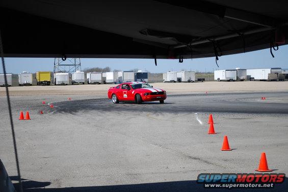 Red Ford Mustang with white stripes and Marlboro decals driving on a track with orange cones