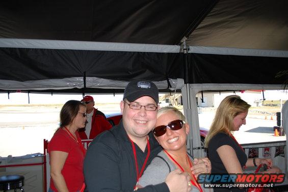 People posing for a photo under a tent with a red car in the background