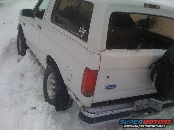 Rear view of a white Ford Bronco stuck in snow, showing a license plate and Ford emblem