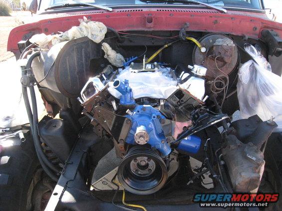 Engine bay with a blue and chrome engine installed. Red truck hood visible