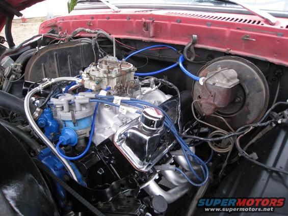 Engine bay with V8 engine, carburetor, and blue spark plug wires. Red painted firewall visible