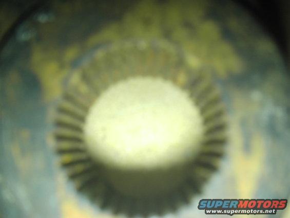 Close-up of a round, ribbed part with a bright center, showing "SUPERMOTORS www.supermotors.net" at the bottom right