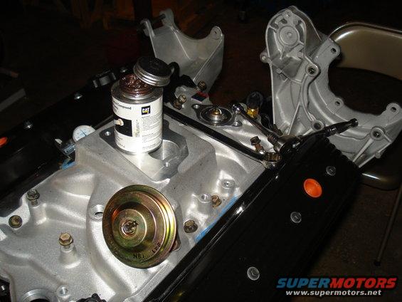 Engine manifold with a can of CAT pipe sealant and various bolts and parts. A small gauge is visible