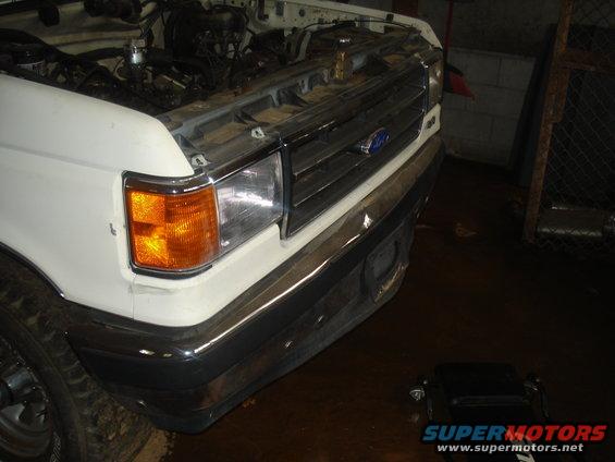 Front of white Ford truck with hood open, showing engine and chrome grille