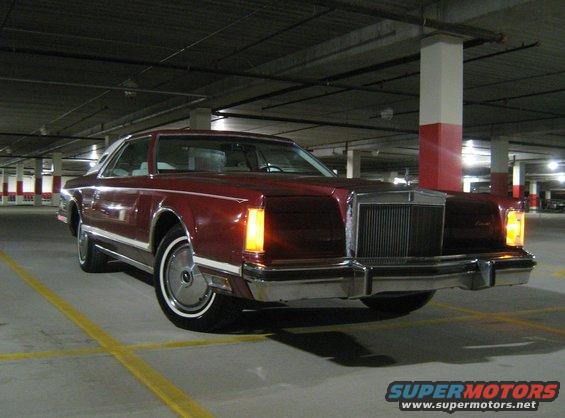Maroon coupe with white vinyl top parked in a parking garage. Front grille and headlights visible