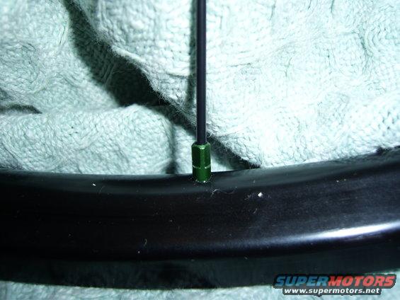 Close-up of a bicycle wheel rim with a green spoke nipple and a black spoke