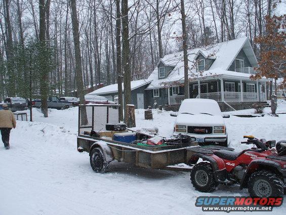 Red ATV and trailer parked in snow near a house