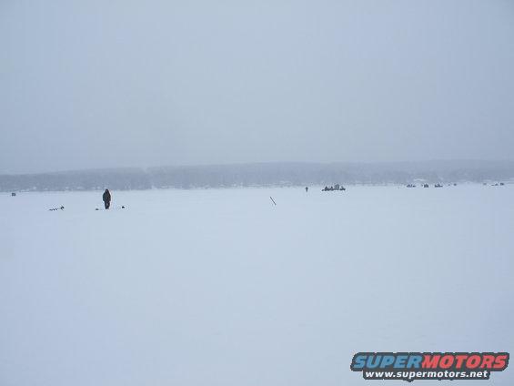 People ice fishing on a frozen body of water with a treeline in the background
