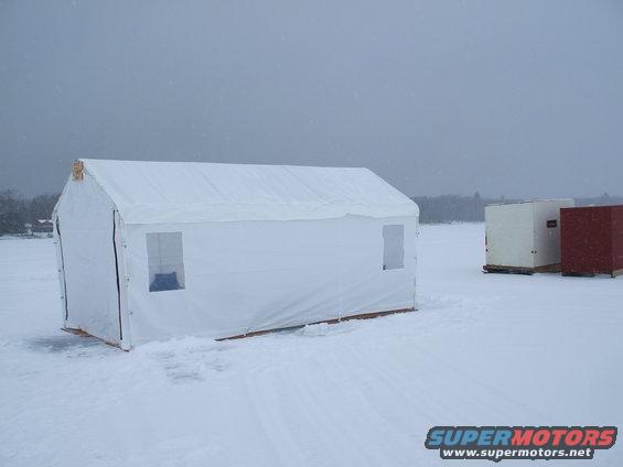 Two ice fishing shelters on a snowy landscape under a cloudy sky