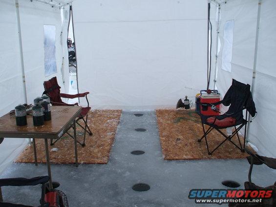Ice fishing tent interior with fishing chairs, propane tanks, and holes in the ice floor