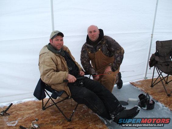 Two men ice fishing inside a tent with fishing rods and gear