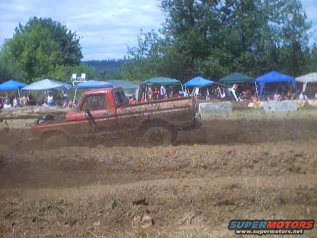Red pickup truck driving through mud with spectators in the background