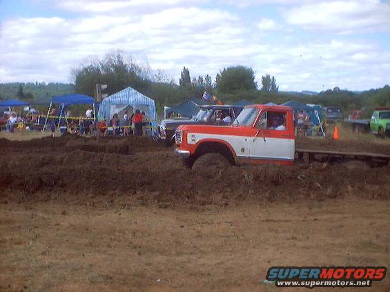 1976 Ford F-100 stuck in mud pit with other vehicles and tents in background