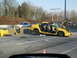 1985 Ford Bronco II - A heavily damaged yellow sedan sits on the highway shoulder with its doors detached and hood open.