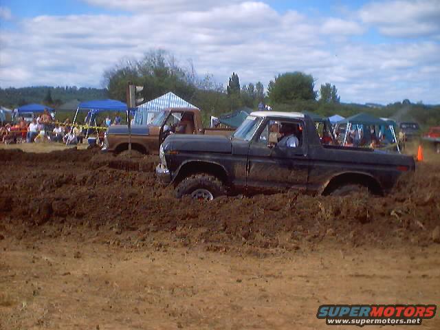 Black Ford F-Series truck stuck in mud, white roof, driver visible