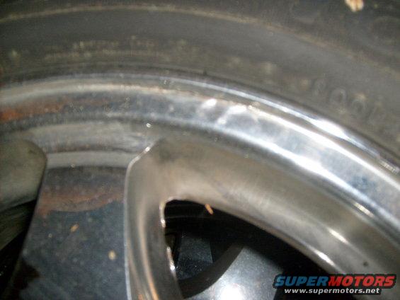 Chrome wheel rim with visible damage and tire tread