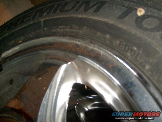 Close-up of a tire with text and a chrome wheel with rust spots