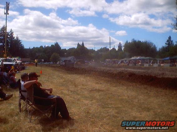 Mud drag racing event with spectators in chairs and tents along the track