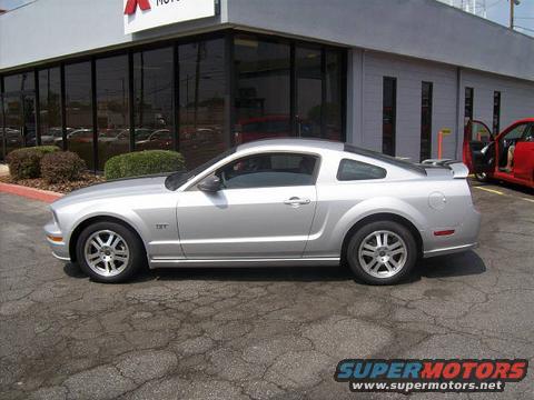 Silver 2005 Ford Mustang parked on cracked asphalt in front of a dealership