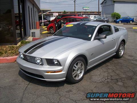 Silver 2005 Ford Mustang GT with black racing stripes parked at a dealership