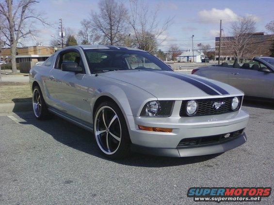 Silver 2005 Ford Mustang with black racing stripes and custom rims, parked outdoors