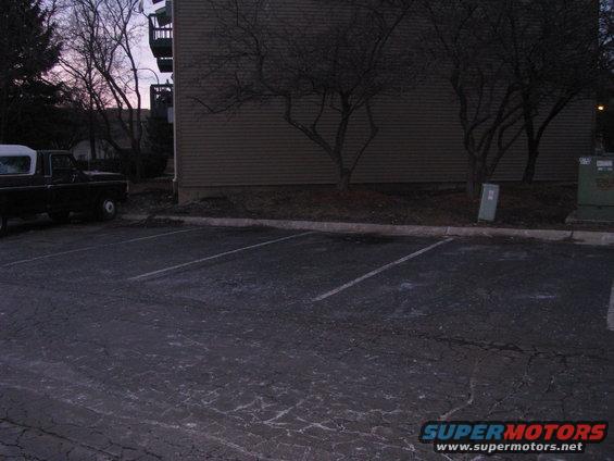 Side view of black pickup truck with white camper shell parked in lot