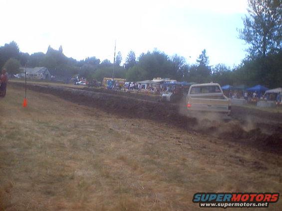 Tan pickup truck driving through mud, rear view. Appears to be from the mid-1970s