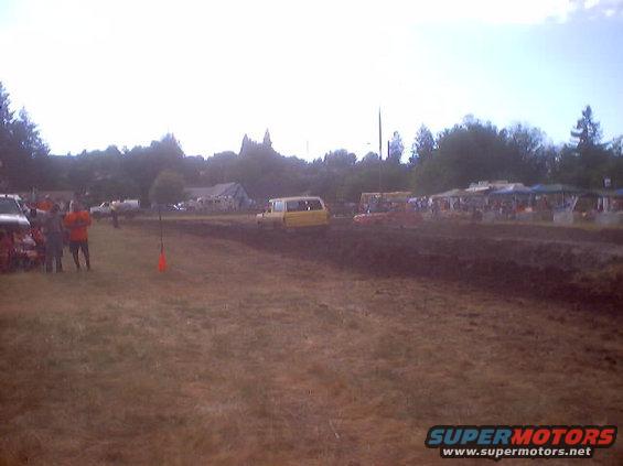 Yellow van on a muddy track with spectators in the background