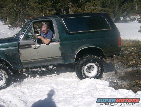 1990 Ford Bronco driving through snow with a man in the driver's seat