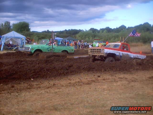 Red and white pickup truck stuck in mud, front view. American flag on antenna