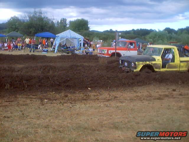 1976 Ford F-100 and an orange and white truck stuck in mud at a drag race