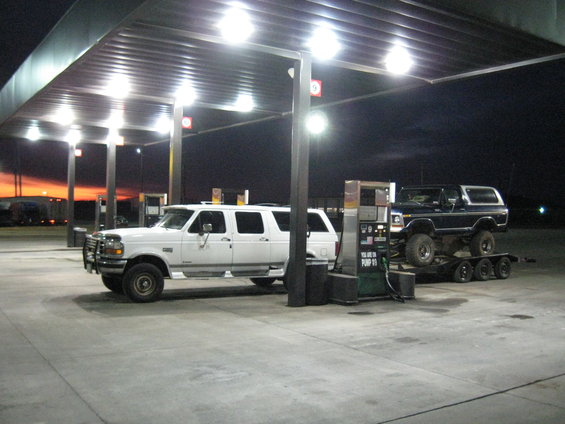 Black Ford Bronco on a trailer at a gas station with a white SUV next to it