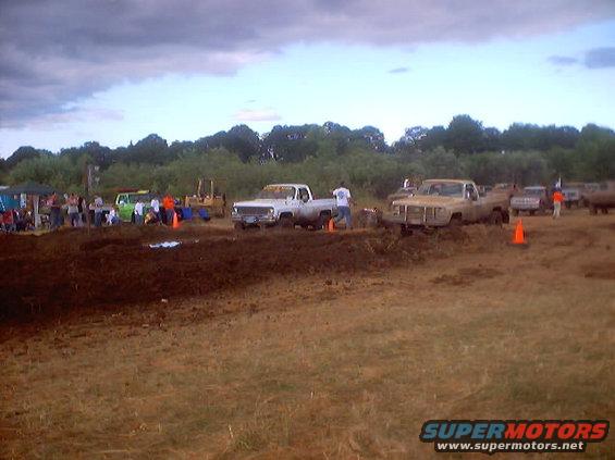Trucks at a mud drag race, with spectators and a bulldozer in the background