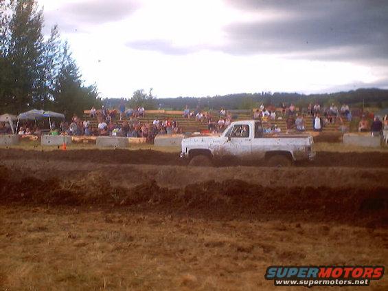 White pickup truck with mud tires driving through a mud pit