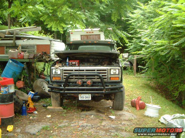 1980 Ford Bronco front view, hood open, parked in a yard with trailers and debris