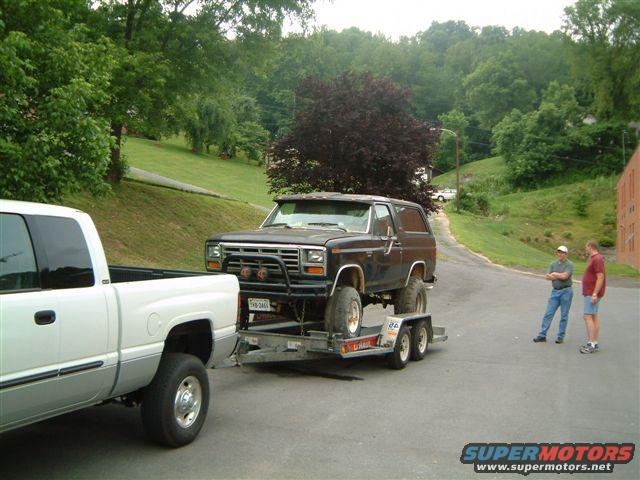 Black Ford Bronco on a trailer towed by a white pickup truck, front view