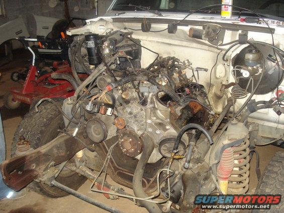 1991 Ford Bronco engine bay with engine partially disassembled, front suspension and wheel visible.
