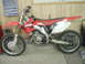 2005 Honda CR125R - A red and white Honda dirt bike is parked indoors, possibly in a garage or workshop.